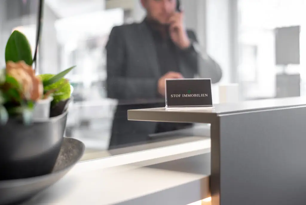 Visitenkarten von Stof Immobilien im Vordergrund mit Marcel Stof, Inhaber, im Hintergrund beim Telefonieren im Maklerbüro in Laichingen